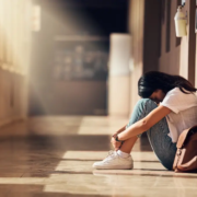 A young adult sitting alone in a hallway in distress, representing rising mental health challenges and mortality trends among young adults in the United States.