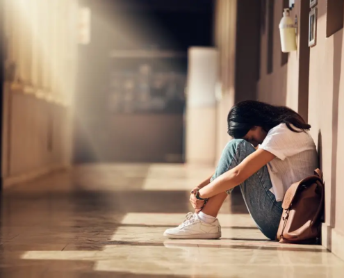 A young adult sitting alone in a hallway in distress, representing rising mental health challenges and mortality trends among young adults in the United States.
