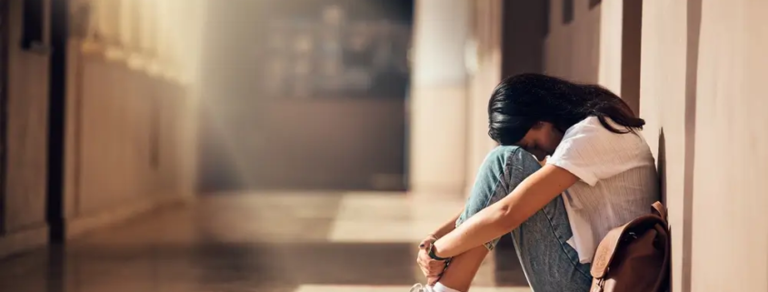 A young adult sitting alone in a hallway in distress, representing rising mental health challenges and mortality trends among young adults in the United States.