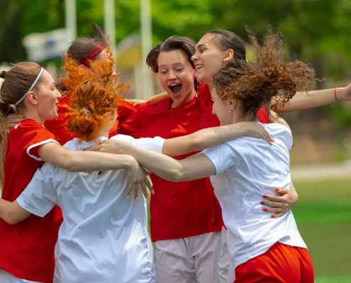 A group of young adults celebrating together on a sports field, symbolizing positive youth development, protective factors, and the importance of prevention and community support in promoting young adult health.