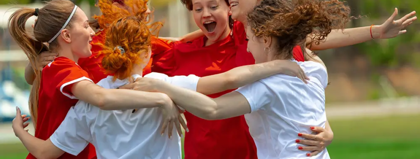 A group of young adults celebrating together on a sports field, symbolizing positive youth development, protective factors, and the importance of prevention and community support in promoting young adult health.
